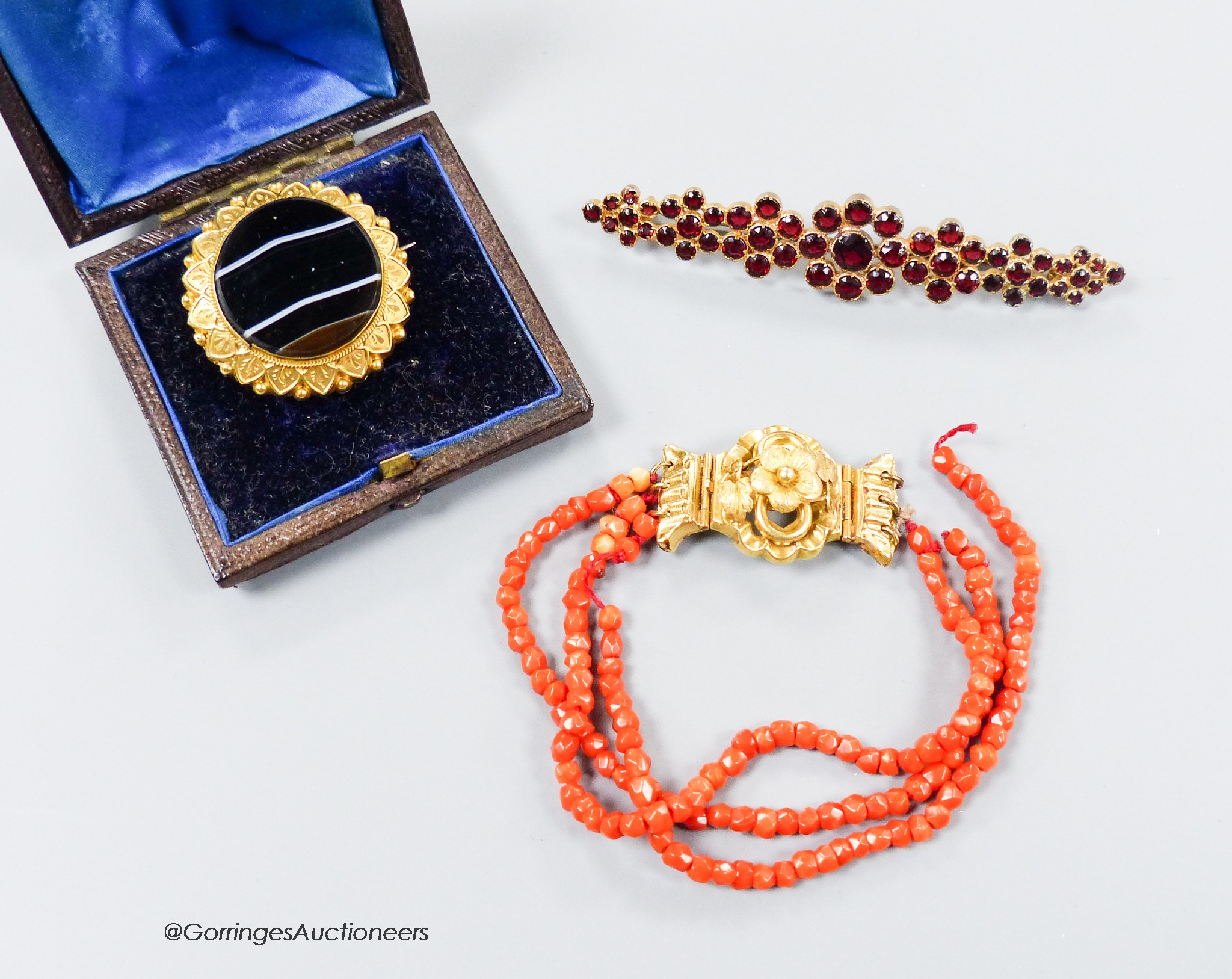 A Victorian yellow metal and banded agate set glazed back mourning brooch, 28mm, gross 8.2 grams, a paste set brooch and a facetted triple strand coral bead bracelet with yellow metal clasp(a.f.) gross 9.6 grams.